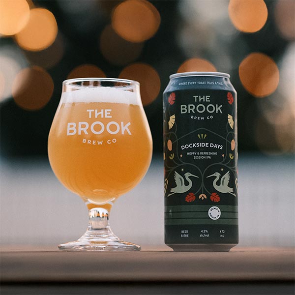 Dockside Days Session IPA can and poured glass of beer from The Brook Brew Co. with bokeh lights in the background