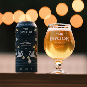From the Lake Lager can and poured glass of beer from The Brook Brew Co. with warm bokeh lights in the background