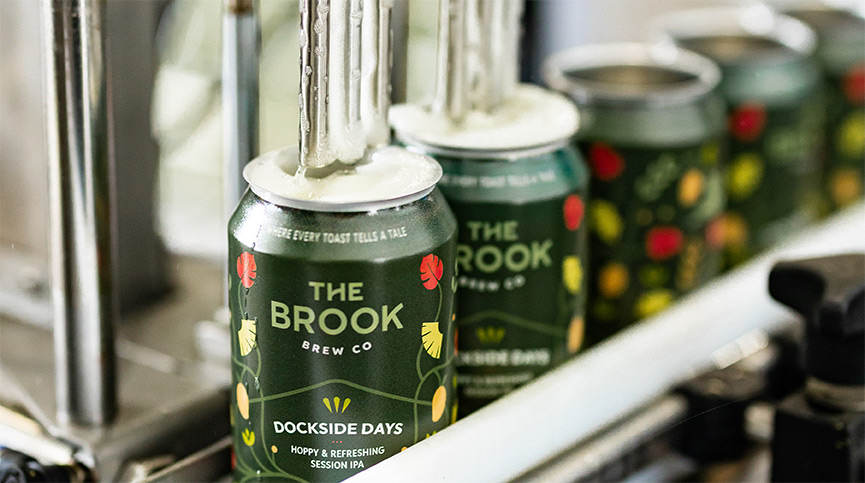 Cans of The Brook Brew Co.'s Dockside Days being filled with beer in a canning line machine.