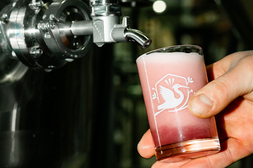 A hand holding a Brook sample glass being filled with beer from a tap in the brewery.