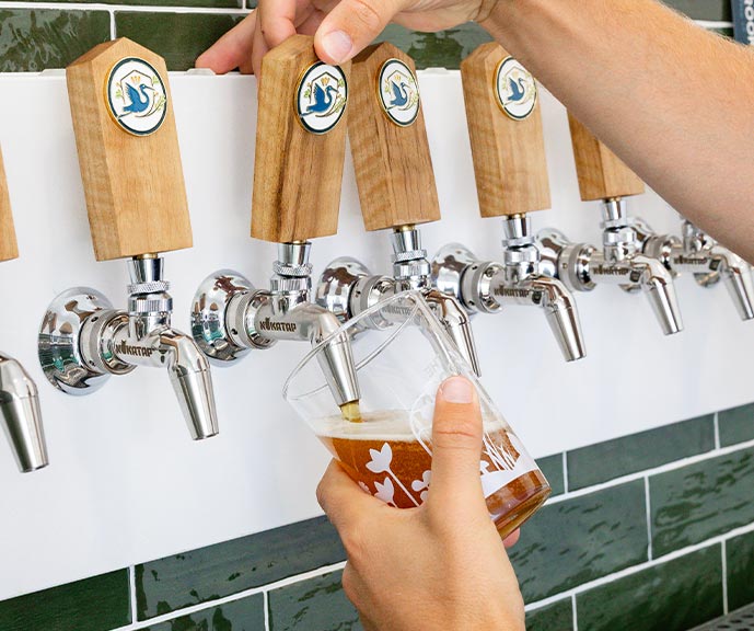 Brook beer being poured from a row of wooden-handled taps into a branded glass.