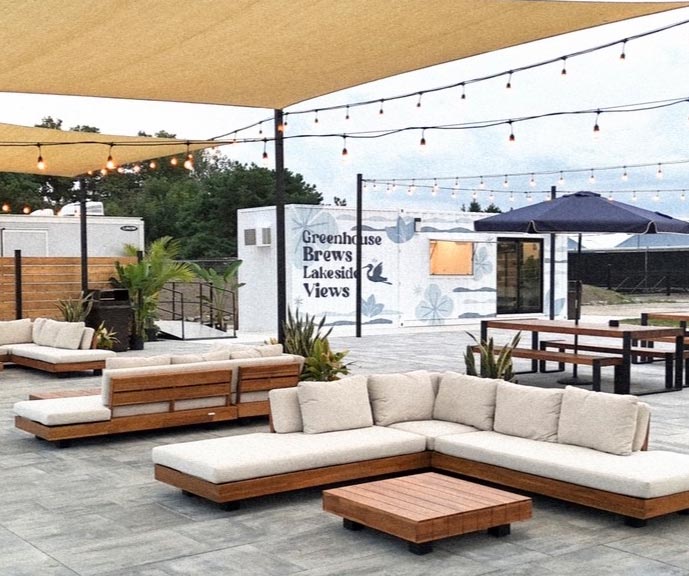 Outdoor lounge seating and picnic tables beneath shade sails and string lights at The Brook Beer Garden.