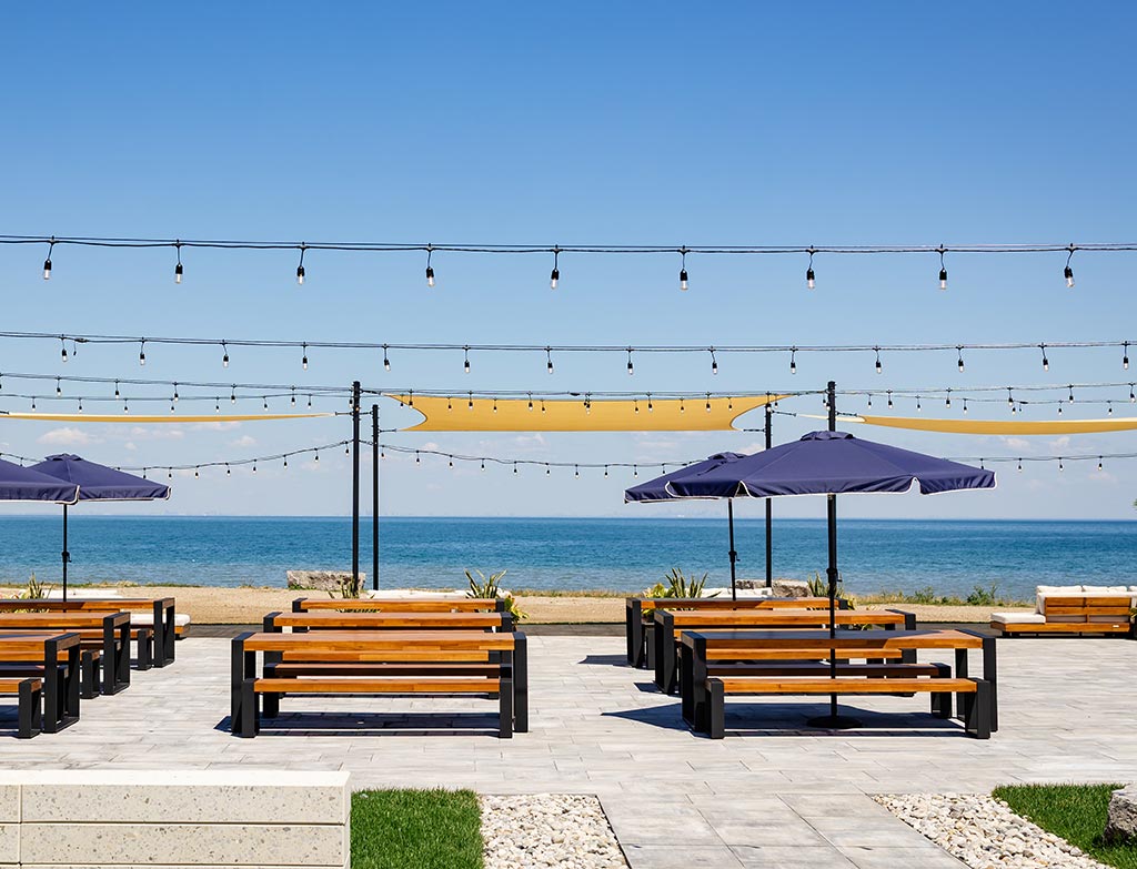 The Brook Brew Co.'s outdoor beer garden patio with wooden picnic tables, umbrellas and string lights overlooking Lake Ontario.