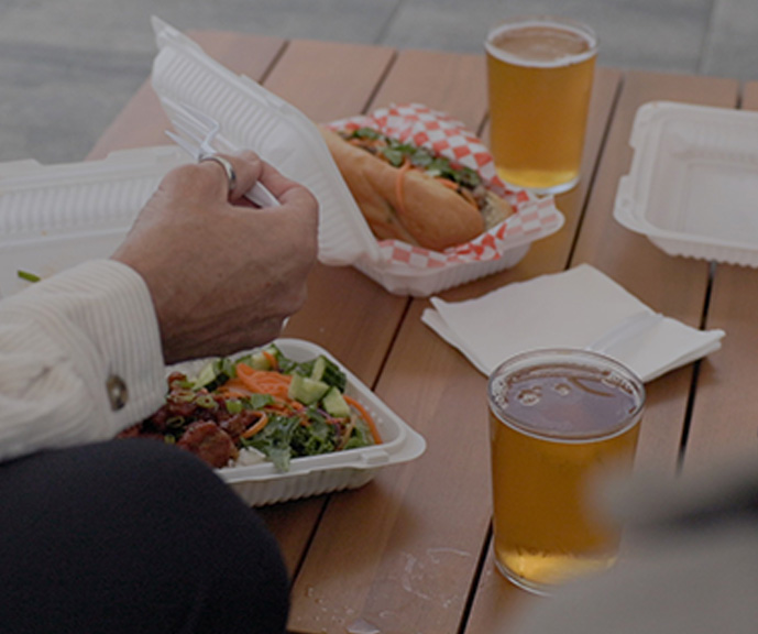 Glasses of beer and takeout food containers filled with food sit on a patio table.